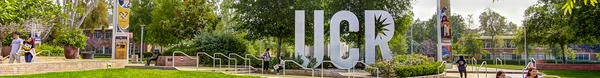 A large sculpture of the UCR logo surrounded by trees and flowering plants